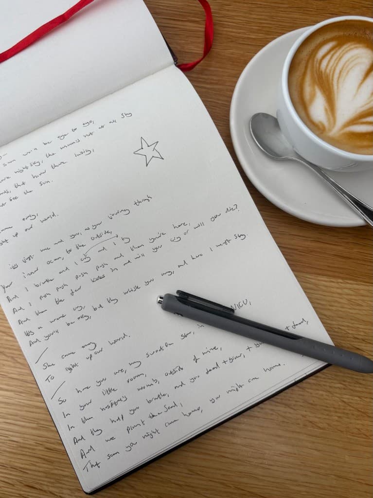 Handwritten song lyrics in a notebook beside a cup of coffee